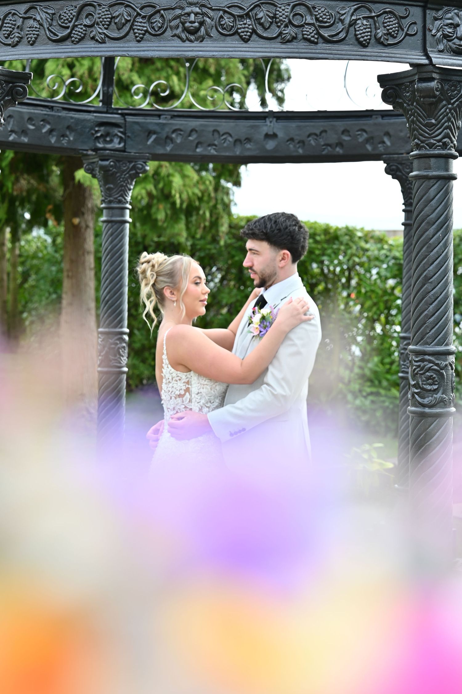 A creative wedding photo captured through a series of wooden fence peepholes showing a bride on a green lawn.