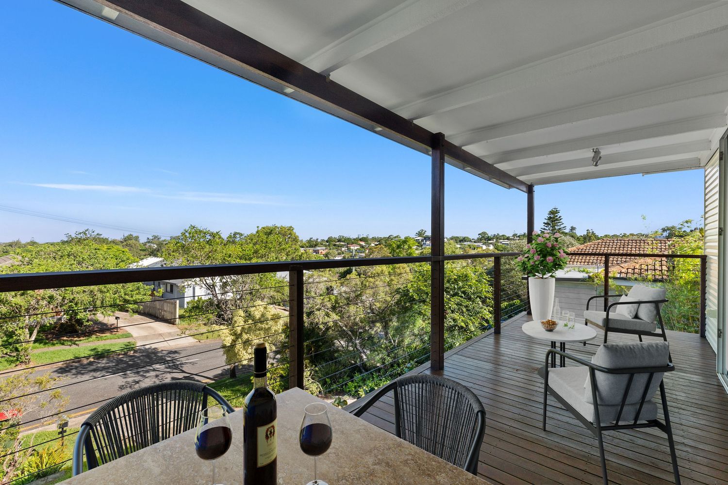 Elevated deck with dining setting and panoramic views of surrounding suburban treetops under blue sky.