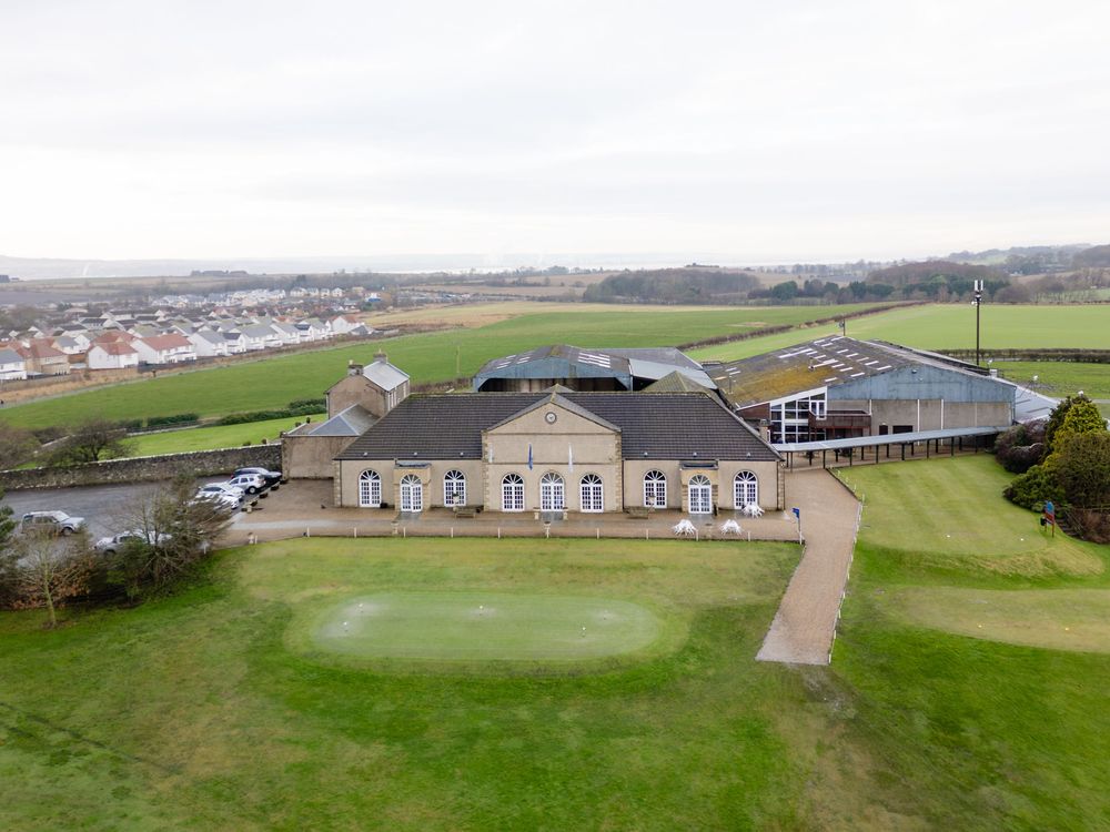 Aerial view of a coastal golf course with clubhouse buildings and green fairways stretching along the shoreline.