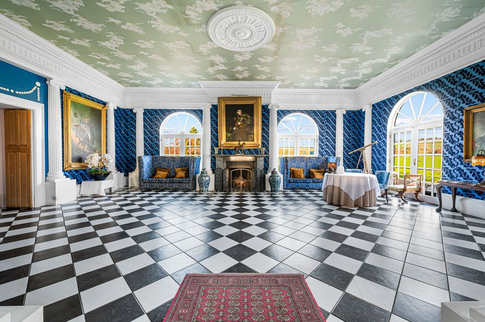 Panoramic view of an elegant hallway with black and white checkered floors and ornate blue walls in a historic building.