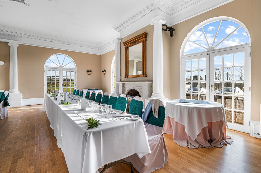 Elegant white event space with arched windows, crown molding, and natural light streaming through multiple windows.