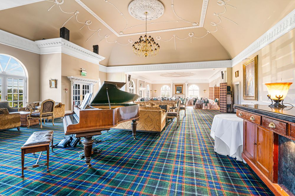 Panoramic view of a grand hotel lobby with blue and green patterned carpet and elegant chandeliers.