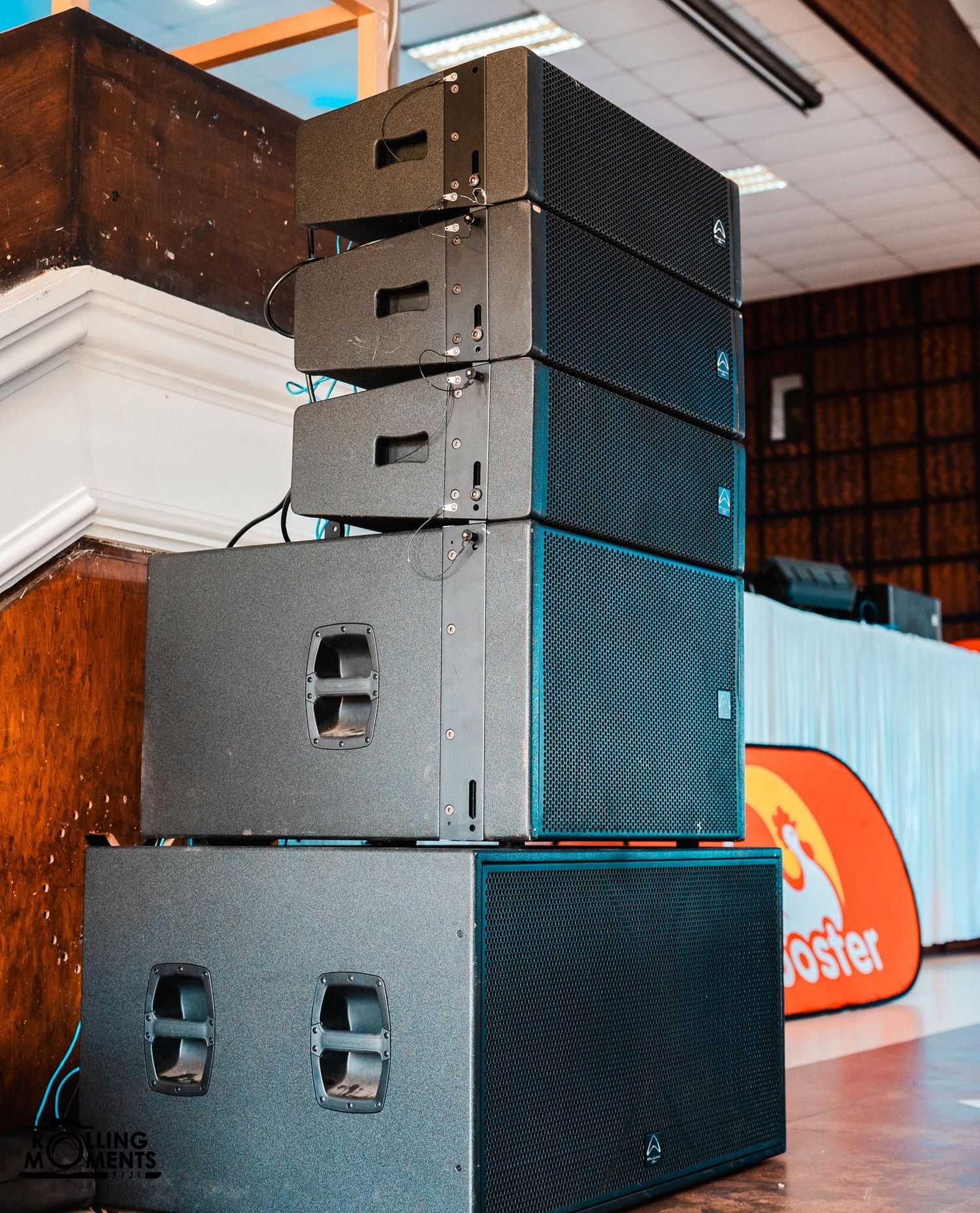 Professional audio speakers stacked vertically against a dark wall with orange accents in the background.