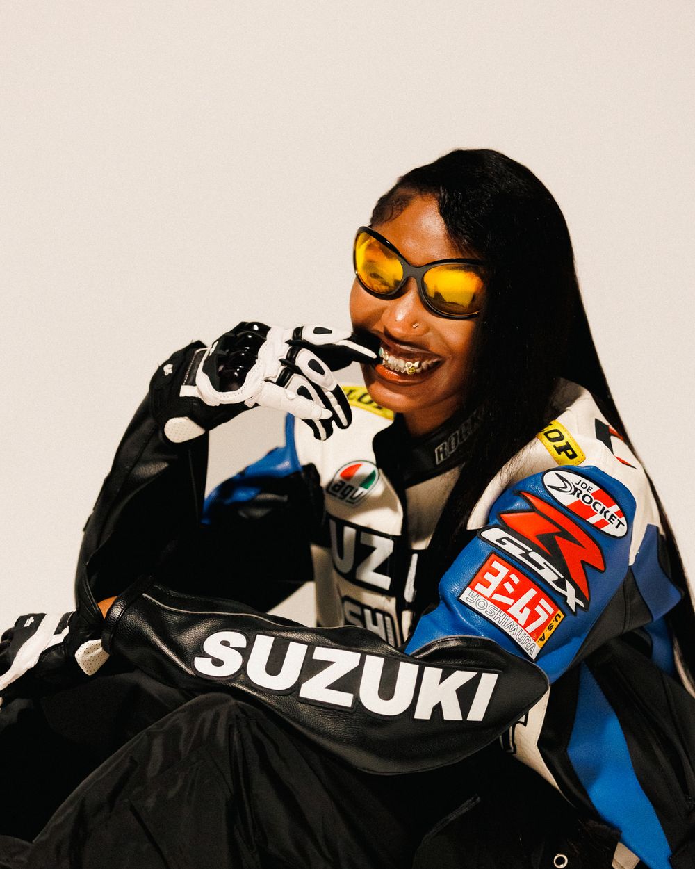 A motorcyclist wearing a Suzuki racing suit and yellow visor helmet shown in a sequence of four similar poses.