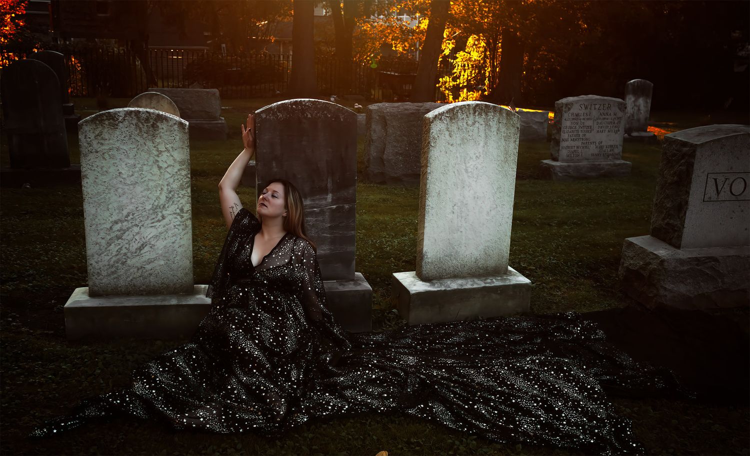 Dramatic photo of person in flowing dress among cemetery headstones at sunset.