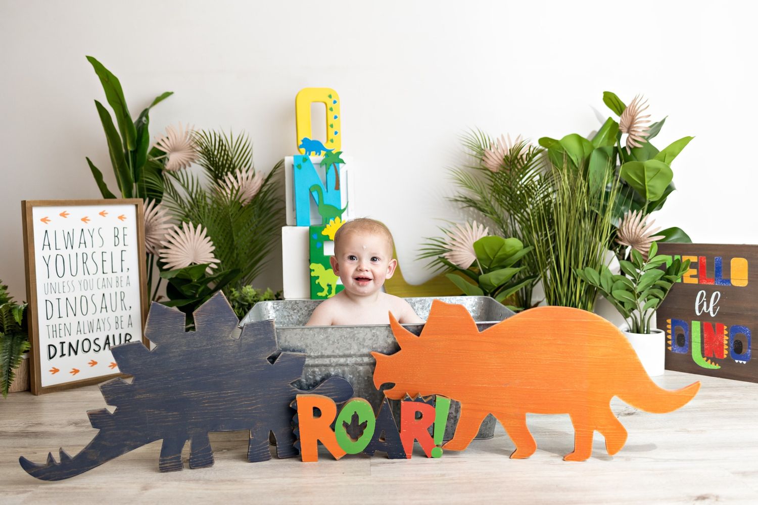 Dinosaur themed photoshoot with colorful wooden cutouts and tropical plants.