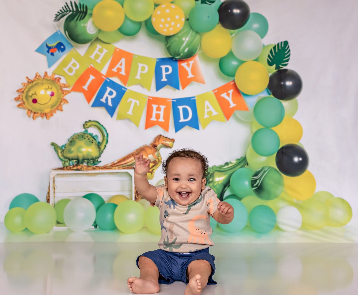 Dinosaur themed first birthday setup with green and yellow balloon arch and decorative banner.