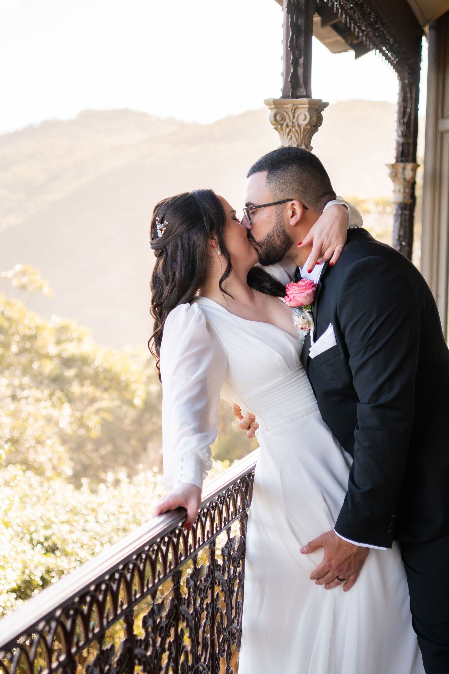 A romantic series of photos showing a couple in wedding attire sharing intimate kisses on a balcony with mountains in the background.
