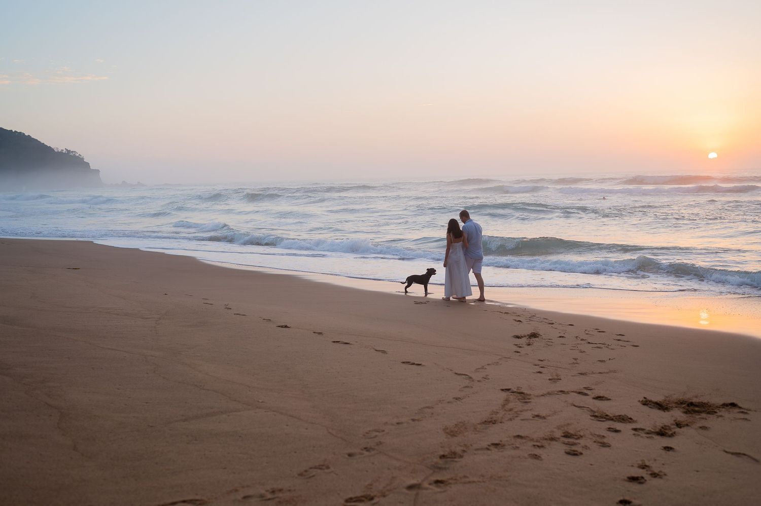 A serene beach at sunset with footprints in the sand and silhouettes walking along the shoreline.