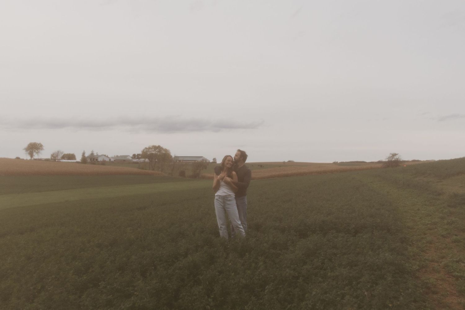 A figure stands in a misty field at dusk with trees on the horizon creating a moody rural landscape.