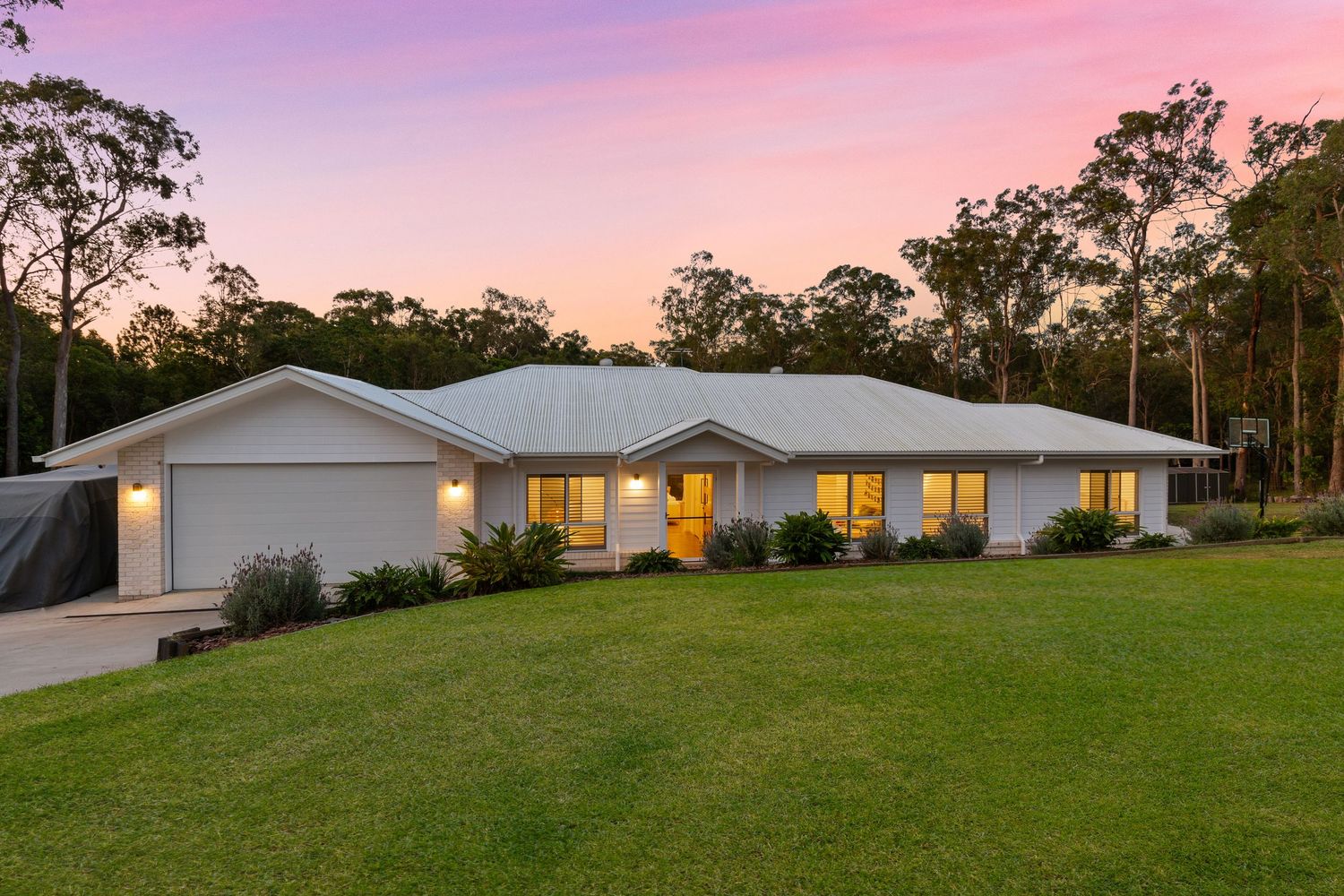 Elegant single-story white home with manicured lawn and eucalyptus trees glowing at sunset.