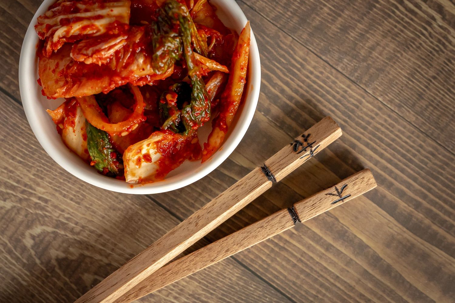 Traditional wooden chopsticks with decorative pattern rest on a black bowl against rustic wooden table surface.