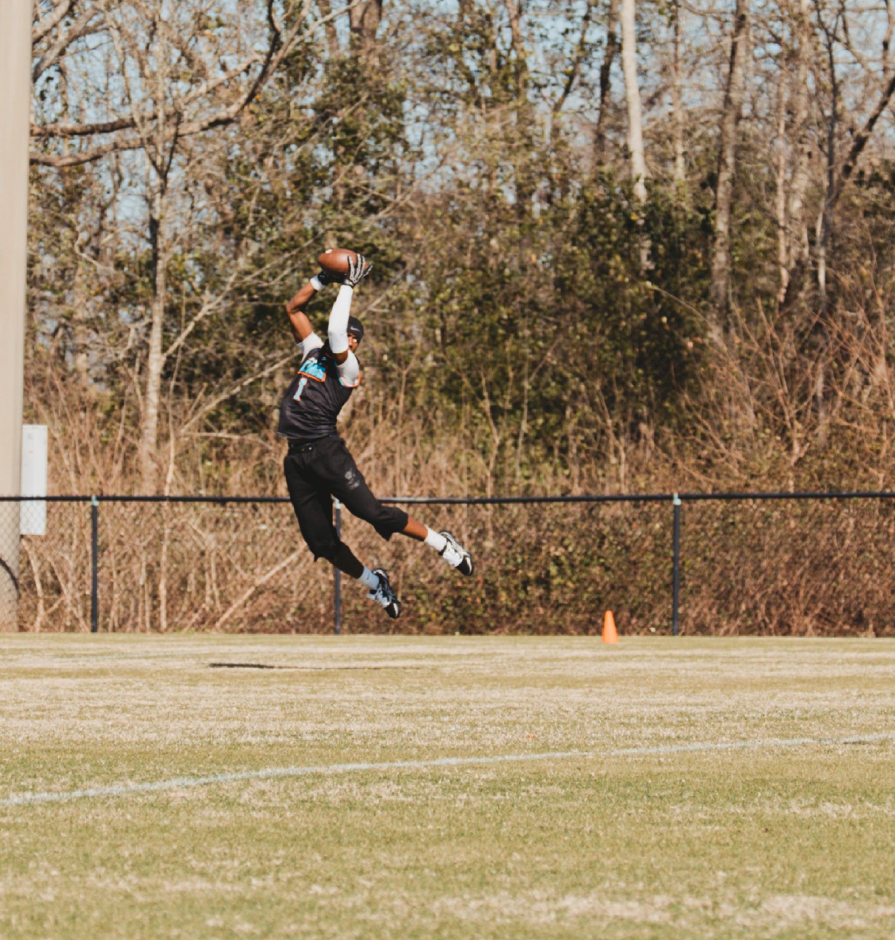 Ultimate frisbee player leaps high into the air to make a catch during an outdoor game on a sunny day.