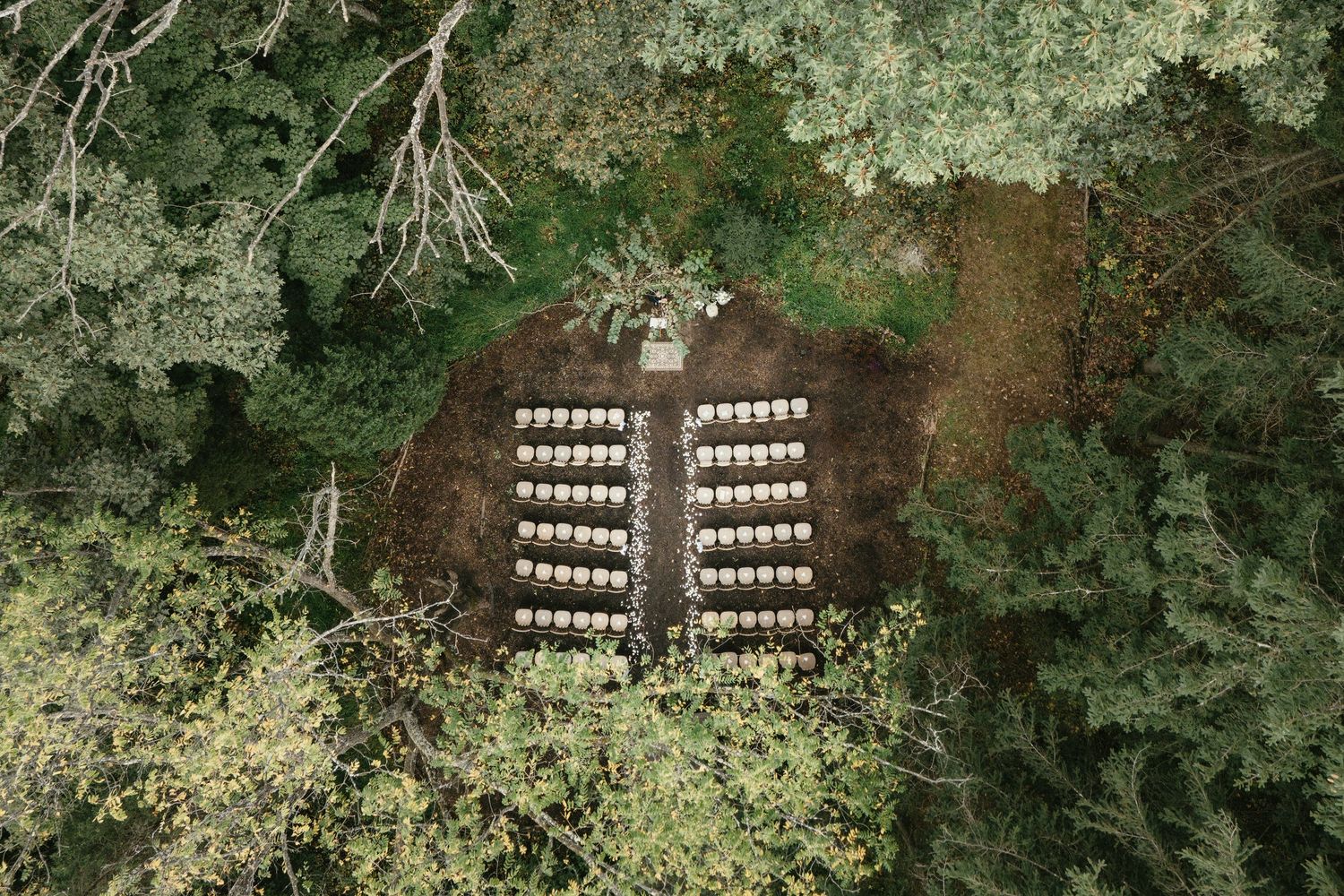 A rustic outdoor wedding venue decorated with wooden benches and lush green foliage creates a natural ceremony setting.