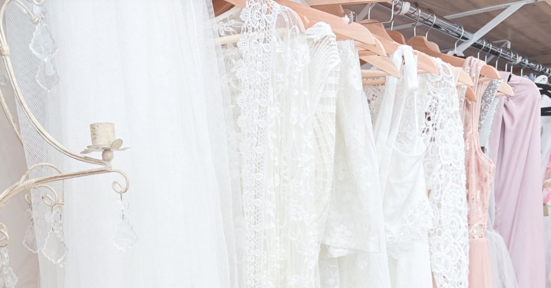 A collection of white and ivory wedding dresses hanging on display racks in a bridal boutique.