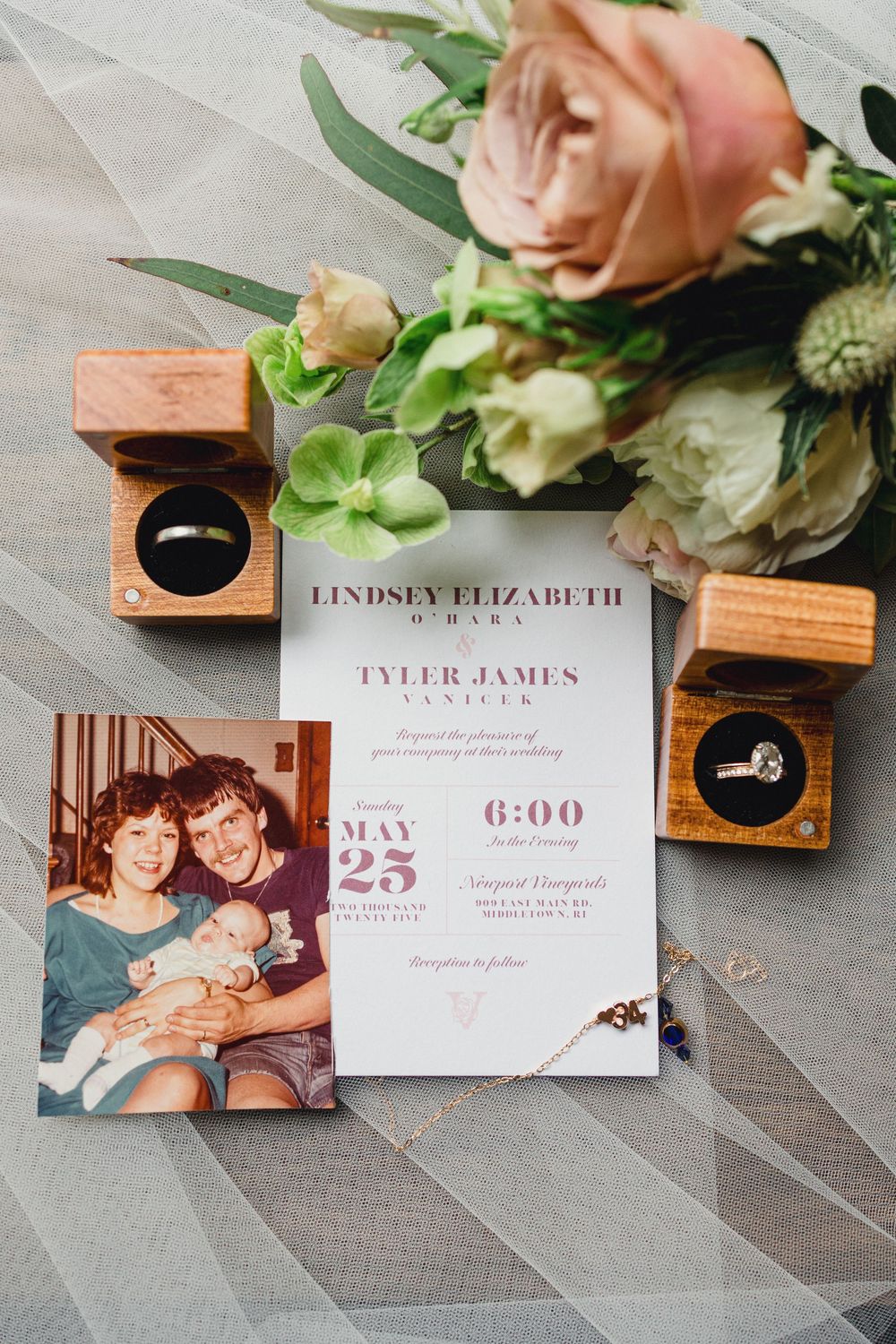 Wedding invitation details and rings displayed with soft pink florals and wooden ring boxes.