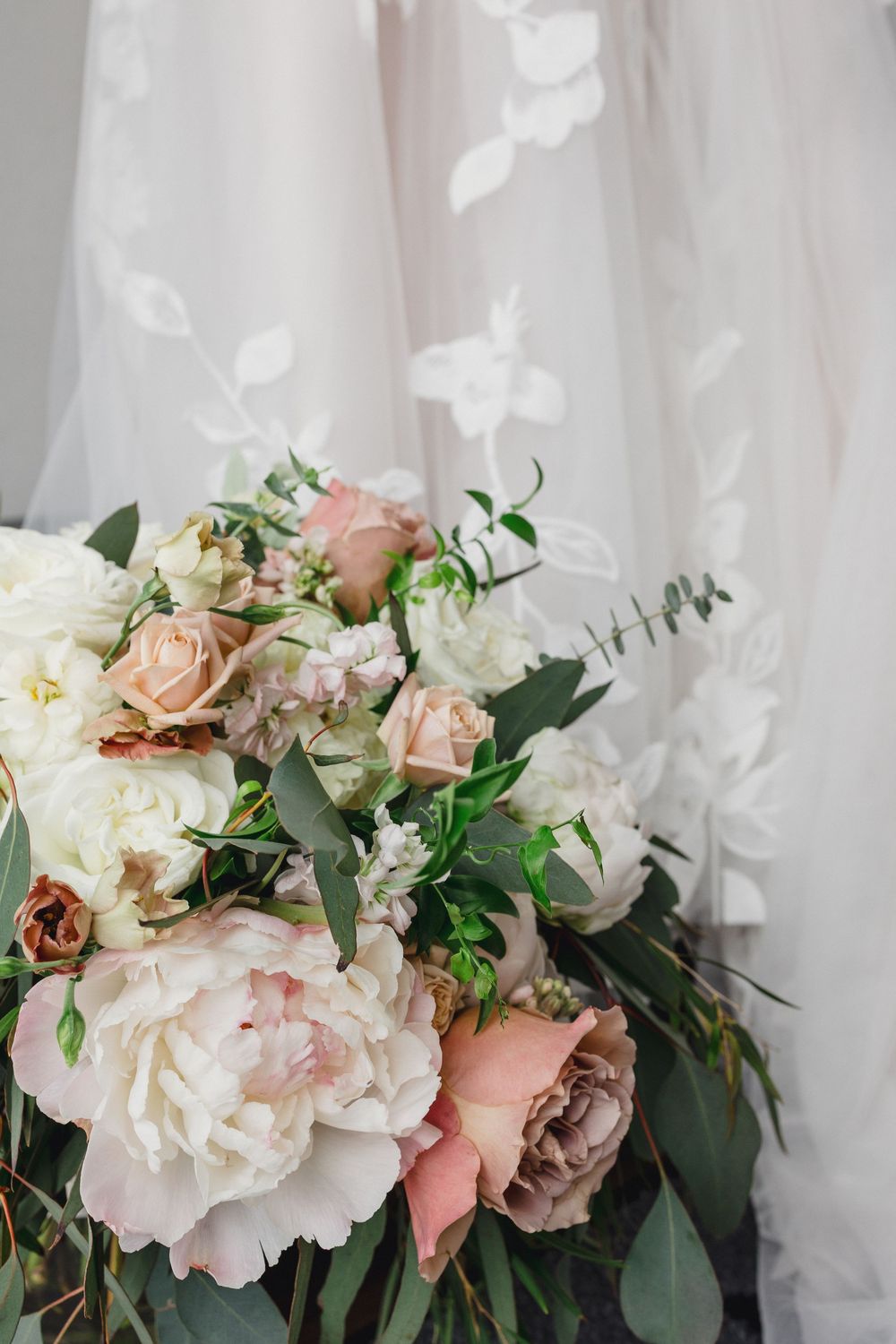 A romantic bouquet of blush pink roses and white peonies with eucalyptus greenery against a light fabric backdrop.
