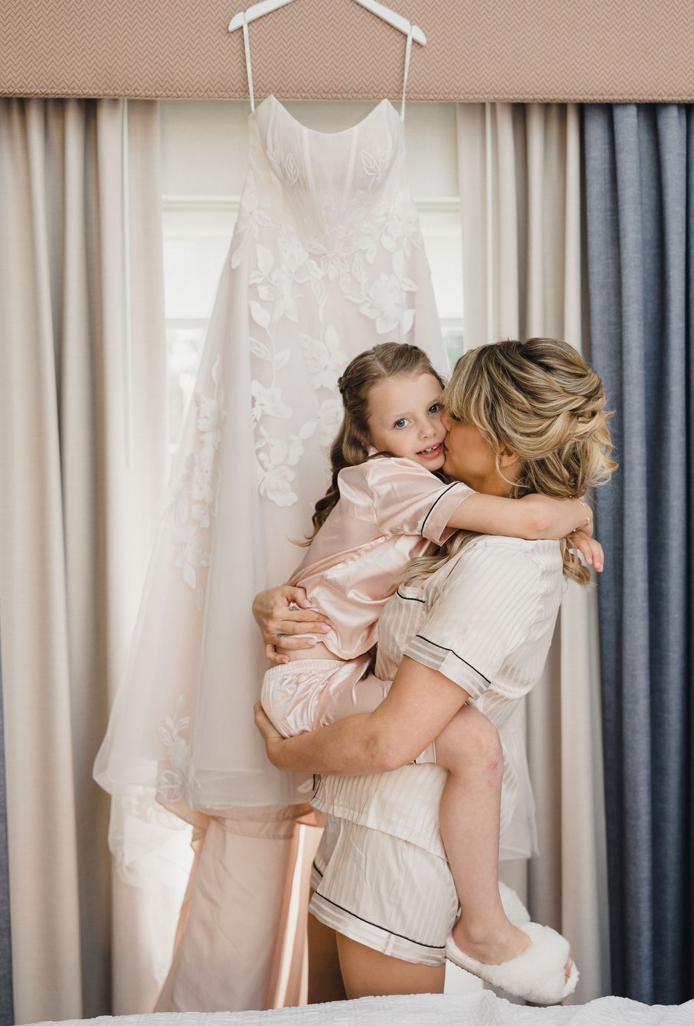 Sweet candid moments captured of a parent and child embracing in a sunlit room with white and blue curtains.
