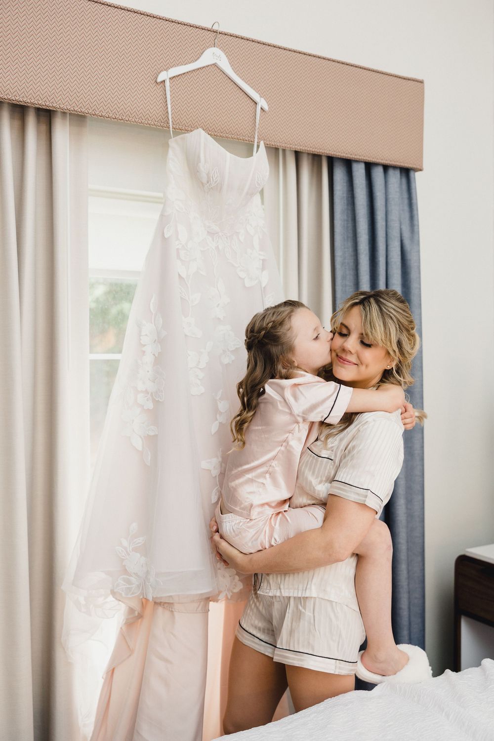 Tender moment shared while getting ready in a sunlit room with wedding dress.