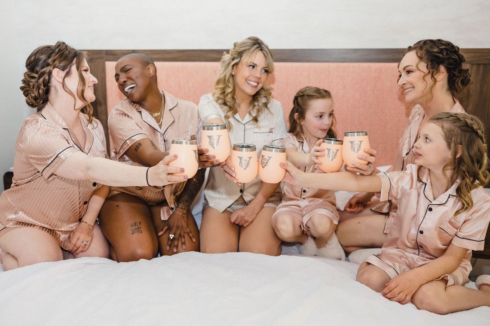 Group wearing matching pink robes relaxing on a bed during pre-wedding preparations.