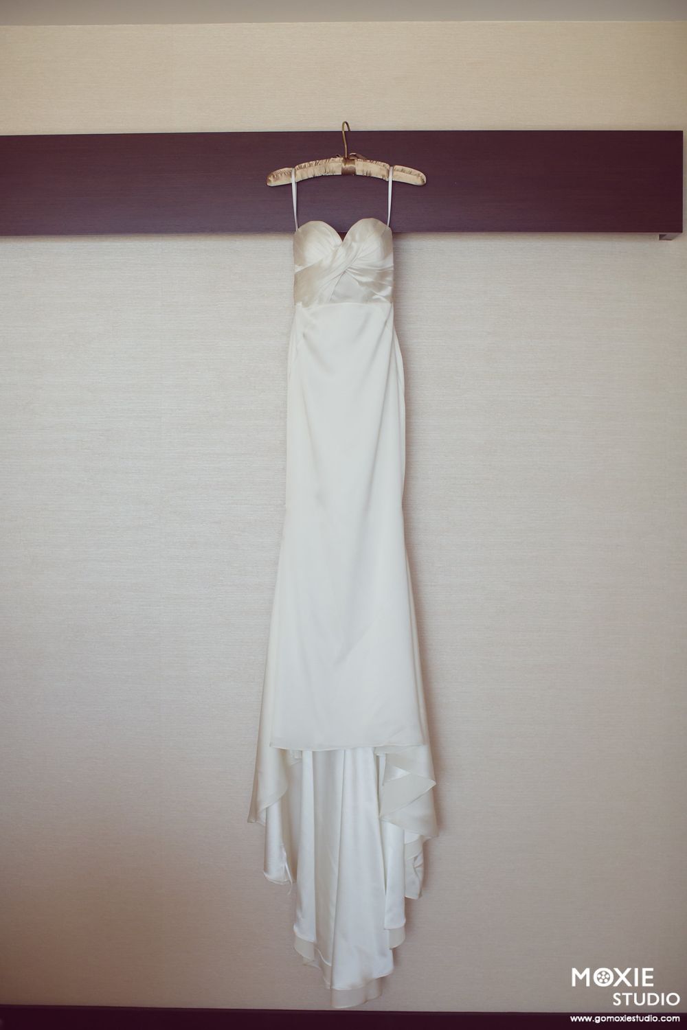 Classic white strapless wedding gown with sweetheart neckline hanging on display against neutral wall.
