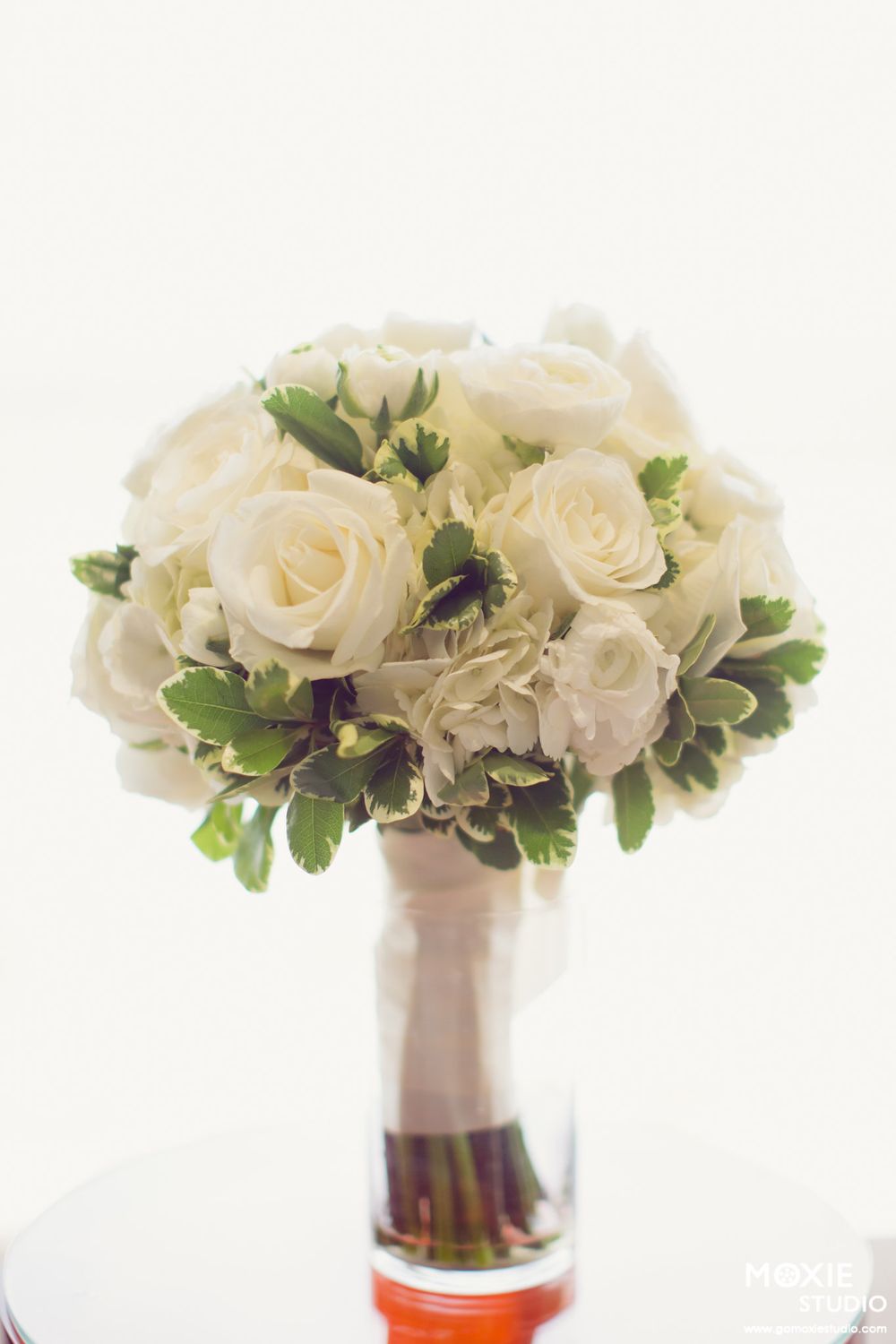 Elegant white rose and greenery wedding bouquets arranged in glass vases against a white background.