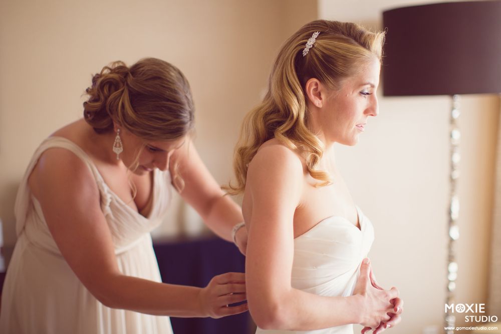 A bride in a white strapless gown getting help with final preparations before the ceremony.