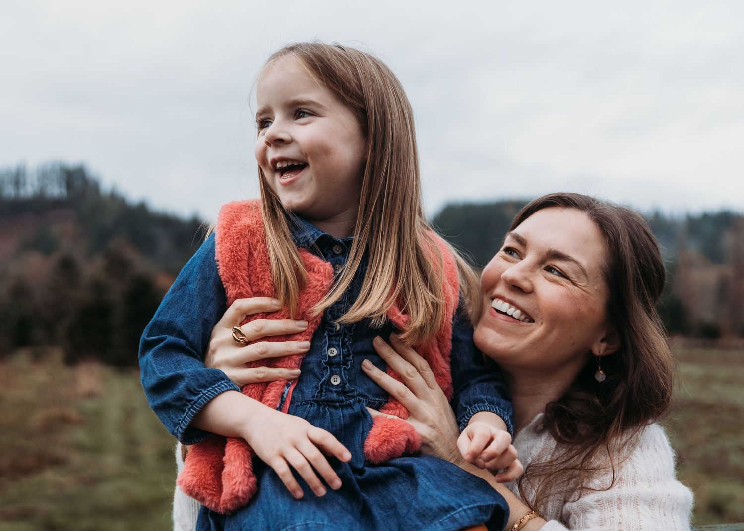 Two people share a joyful moment together outdoors in a natural setting with mountains in the background.