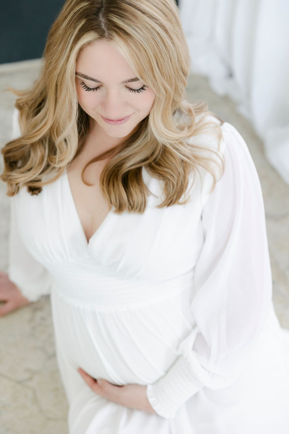 Woman in white robe sitting in soft natural light during an intimate indoor portrait session.