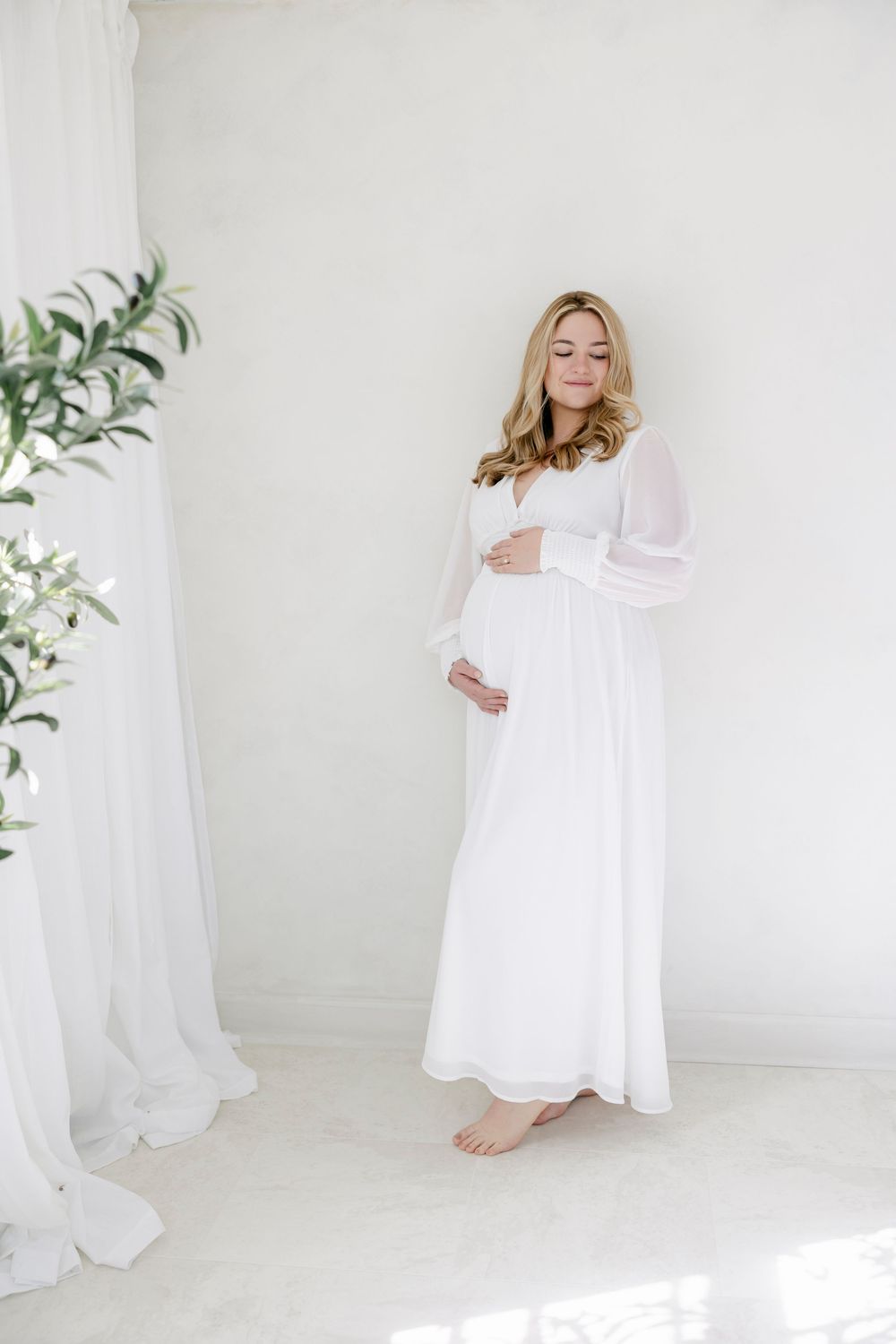 A series of ethereal maternity photos in white featuring a woman in a flowing dress against a bright minimalist backdrop.