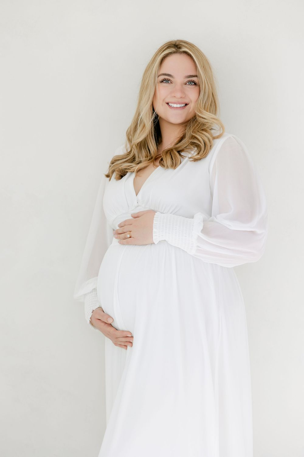 A series of four maternity photos showing a woman in a flowing white dress against a light background.