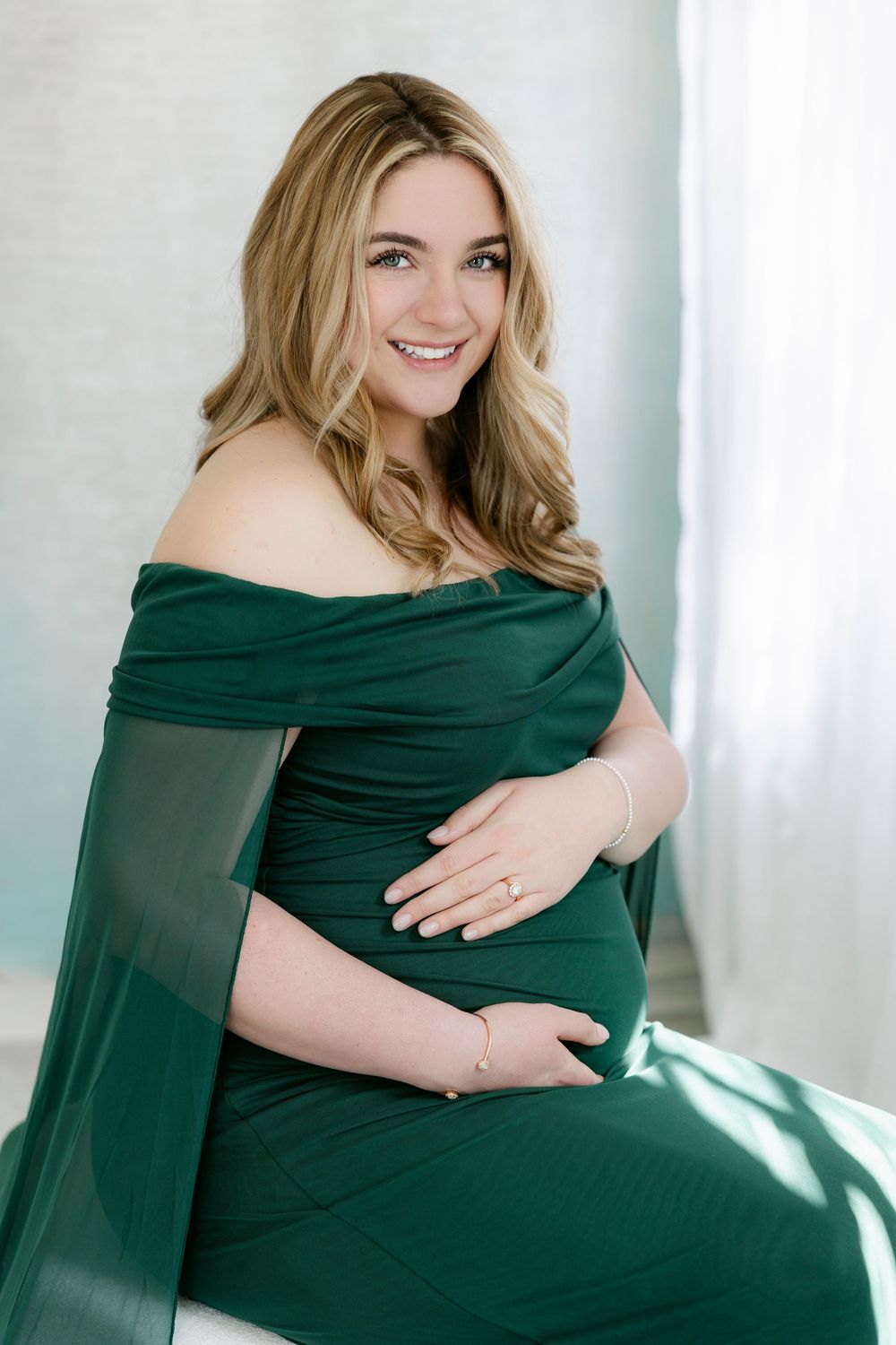 Maternity photo series showing a woman in a dark green dress against a white background.