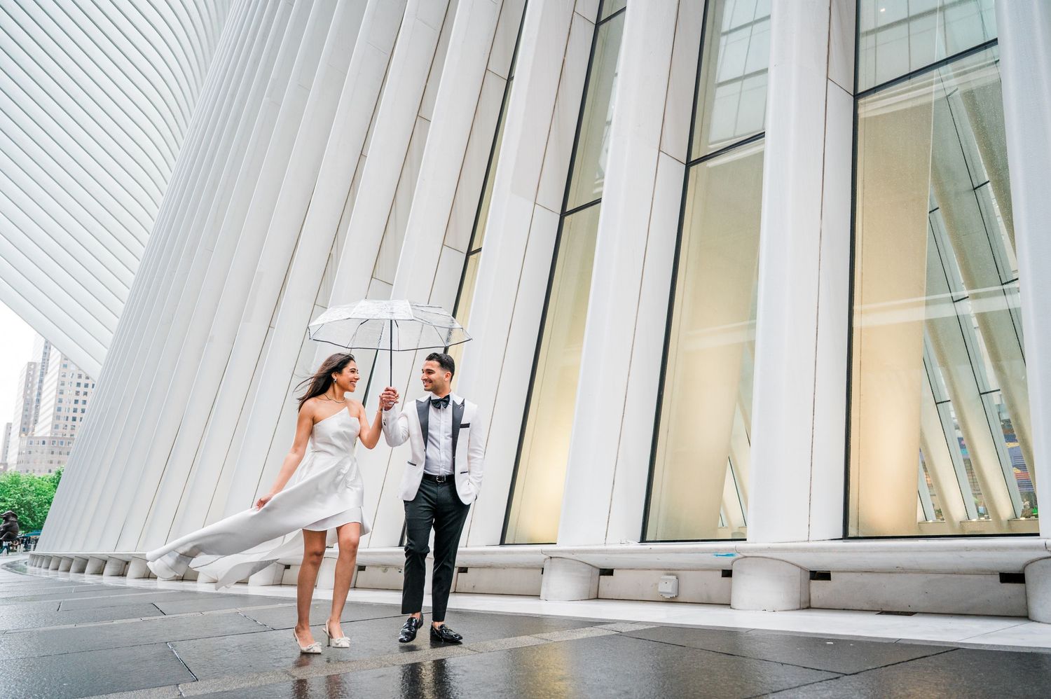 Couple in formal attire stands in modern white architectural space with angled walls and natural lighting.