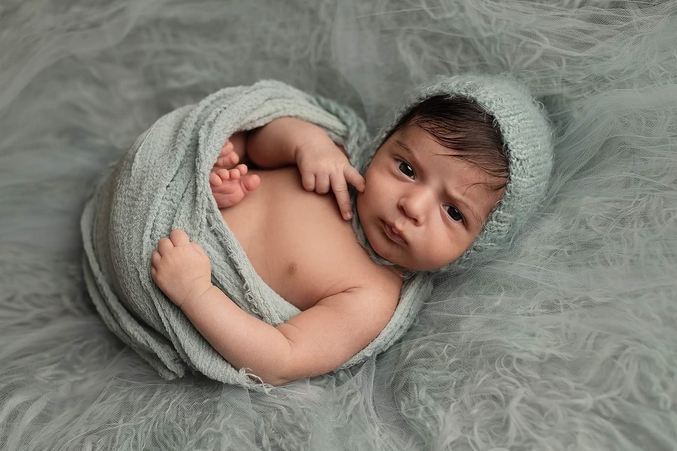 A sleeping newborn baby wrapped in soft gray fabric lies peacefully on a plush gray blanket. Elizabeth Lang Photography Surrey