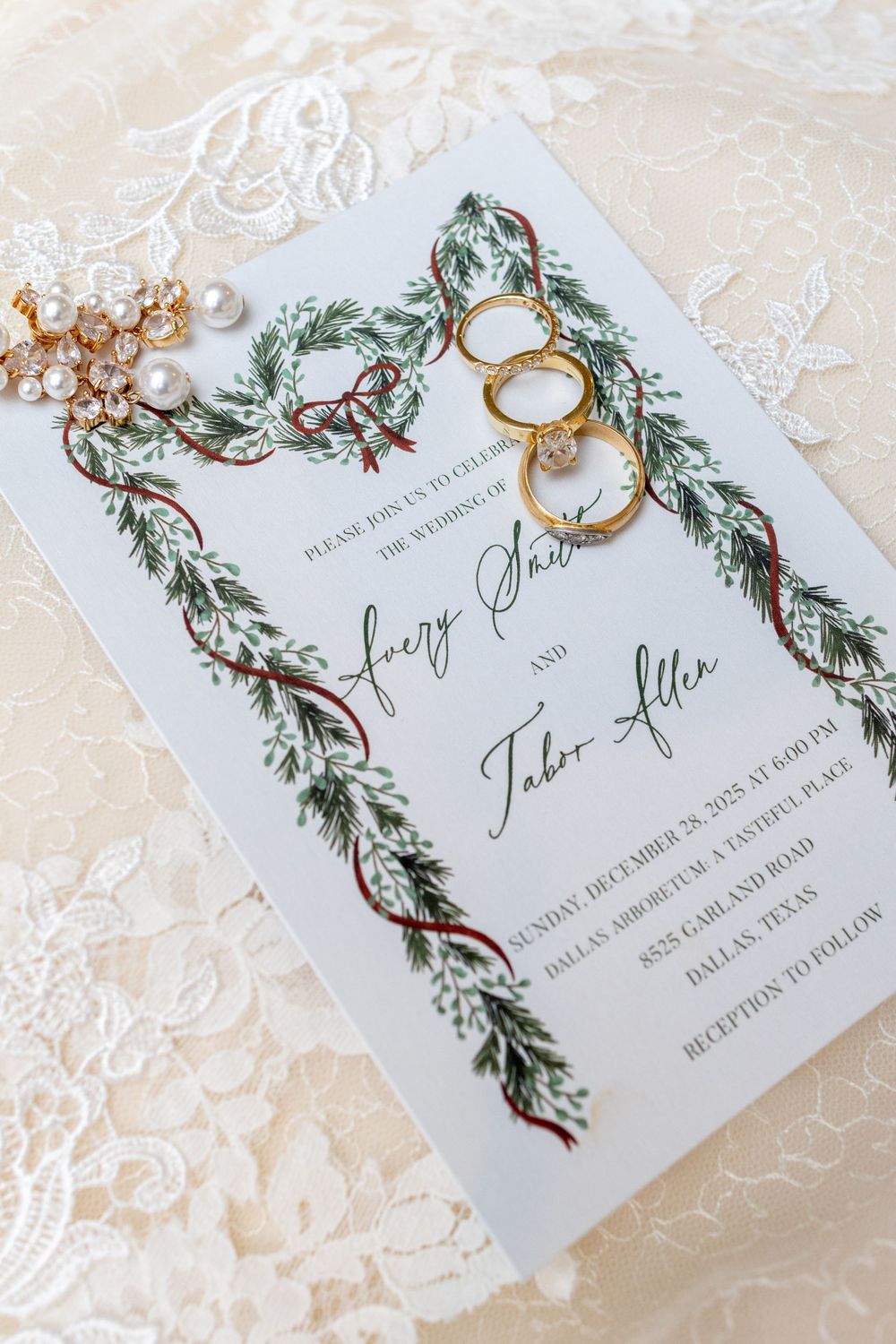 Wedding invitation cards with elegant greenery garland designs and gold rings displayed on a light textured surface.
