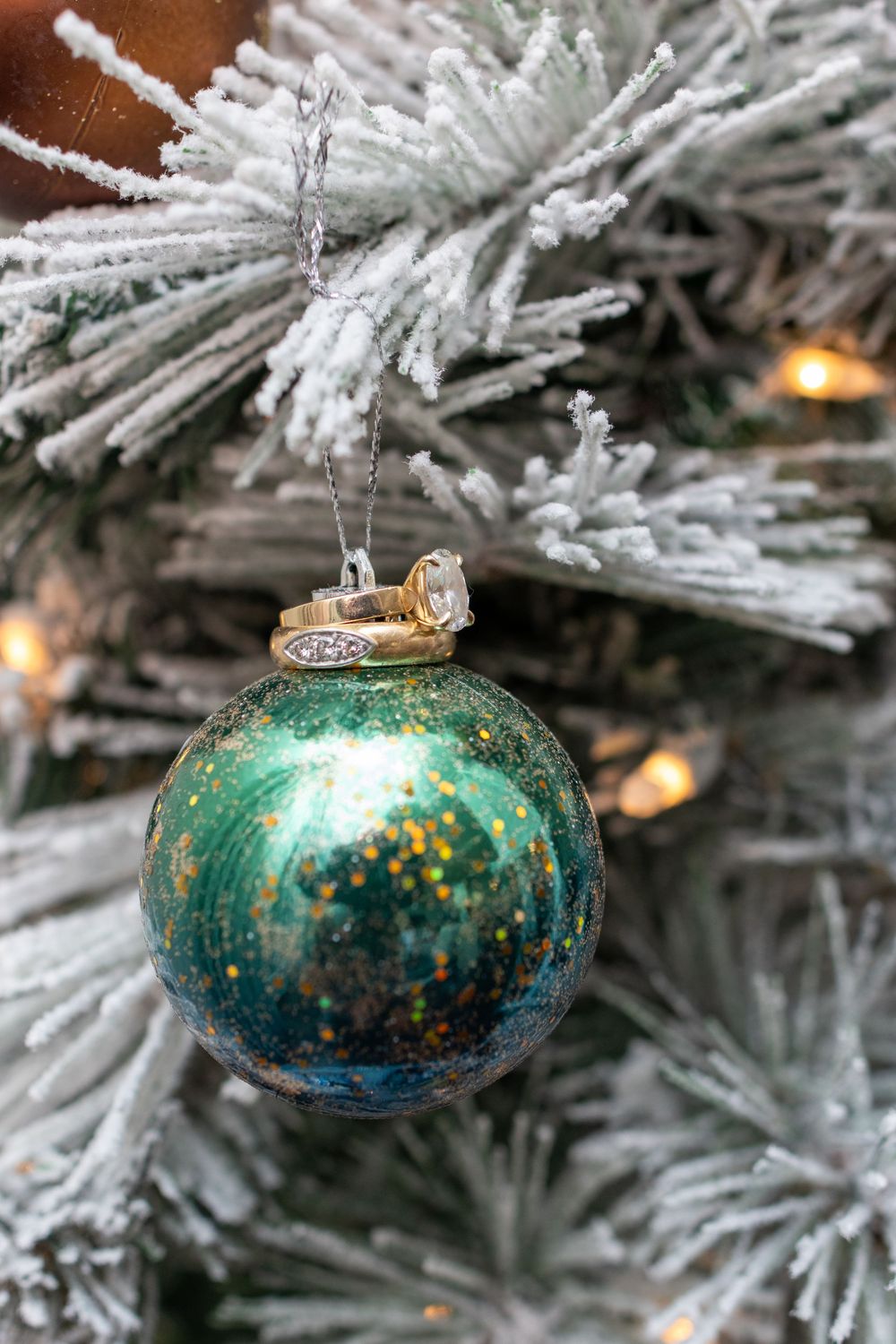 Vintage teal glass Christmas ornaments with gold speckles hanging on a frosted white artificial tree branch.