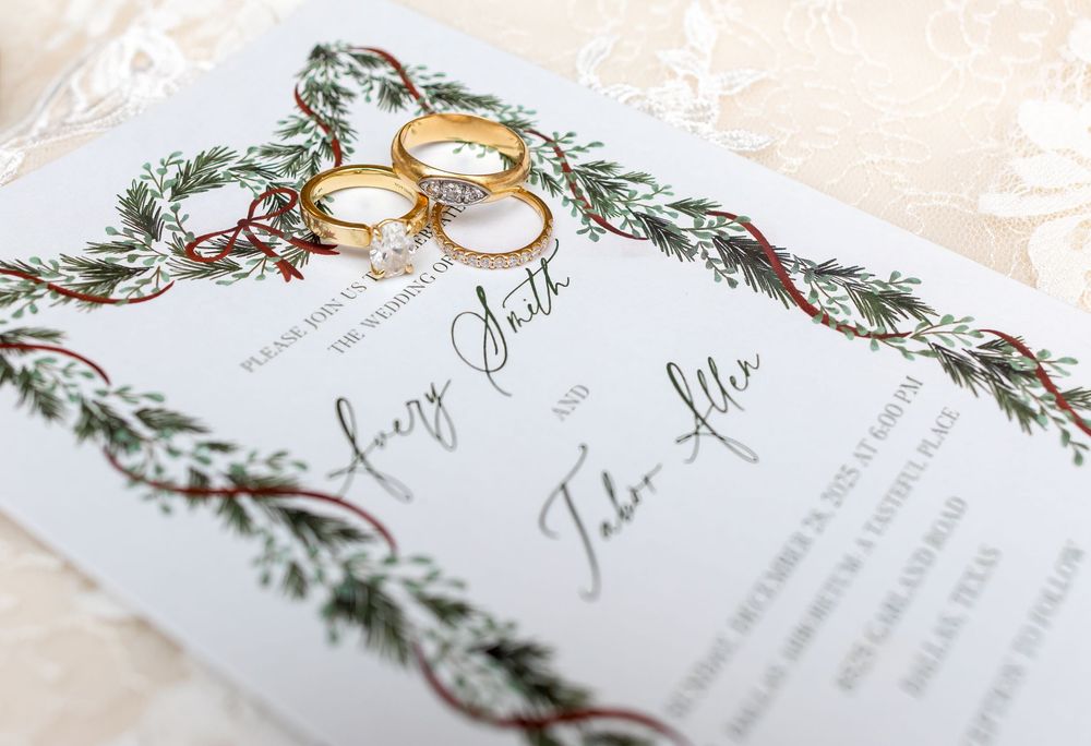 Elegant wedding invitation with delicate floral greenery and gold ring design details on white paper.