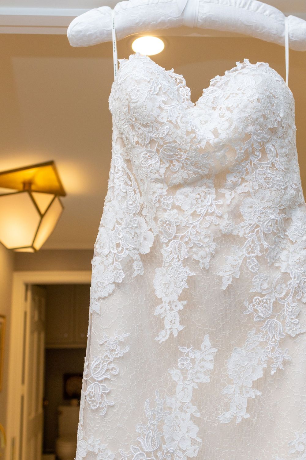 Close up detail of delicate white lace and beadwork on a wedding dress bodice with soft interior lighting.