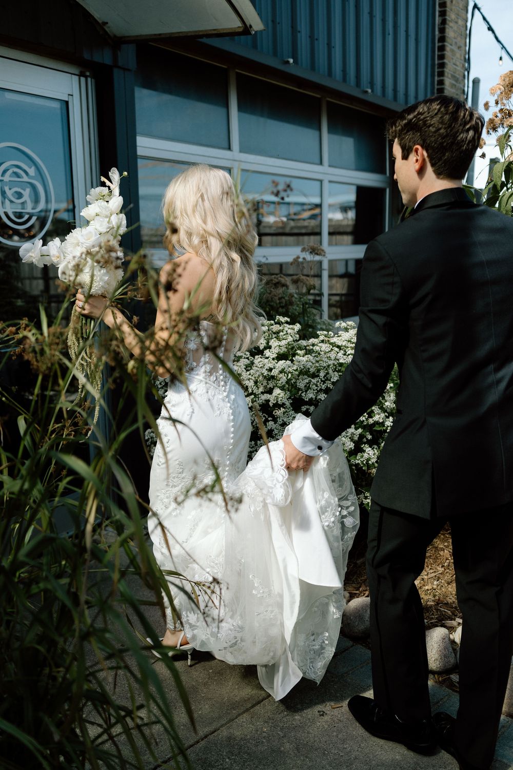 Couple walking through a garden path with white floral arrangements.
