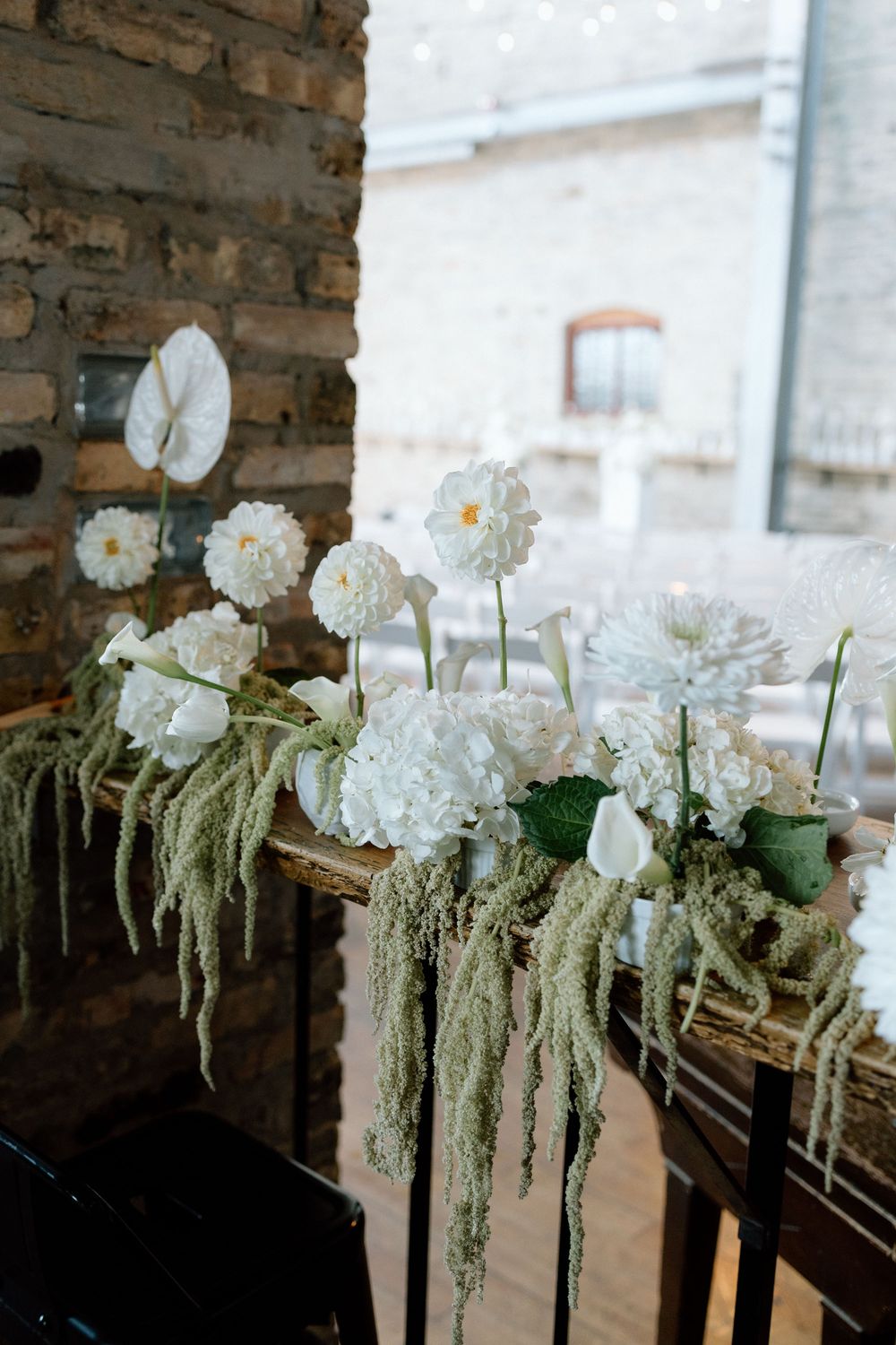 White floral arrangements with cascading greenery decorate a rustic wooden railing.