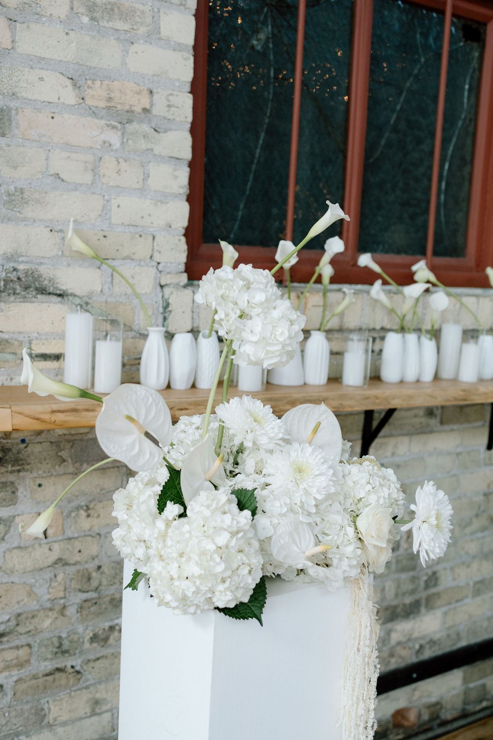 White floral arrangements in white vases displayed along a stone wall.