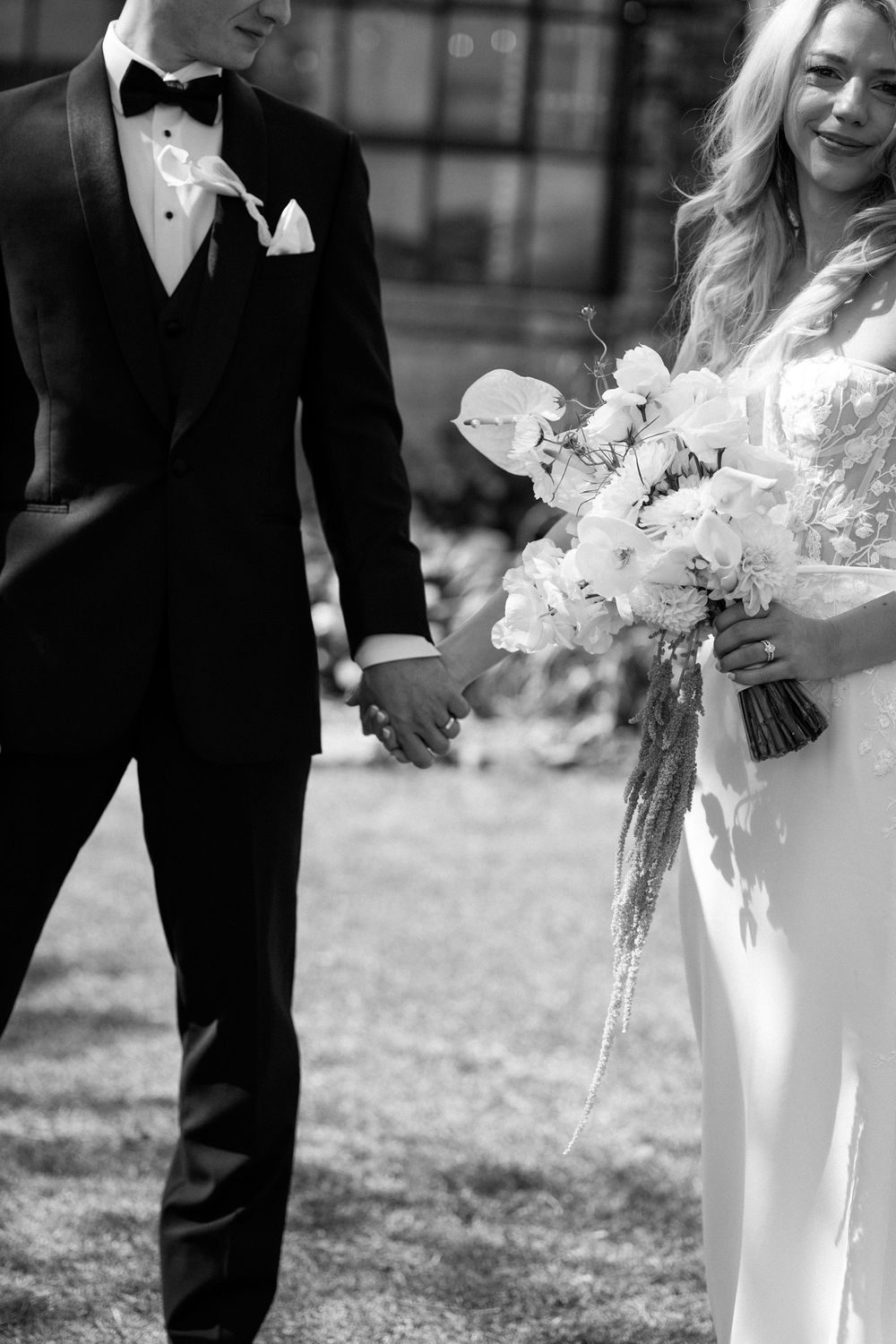 Elegant couple in wedding attire standing together with white floral bouquet.
