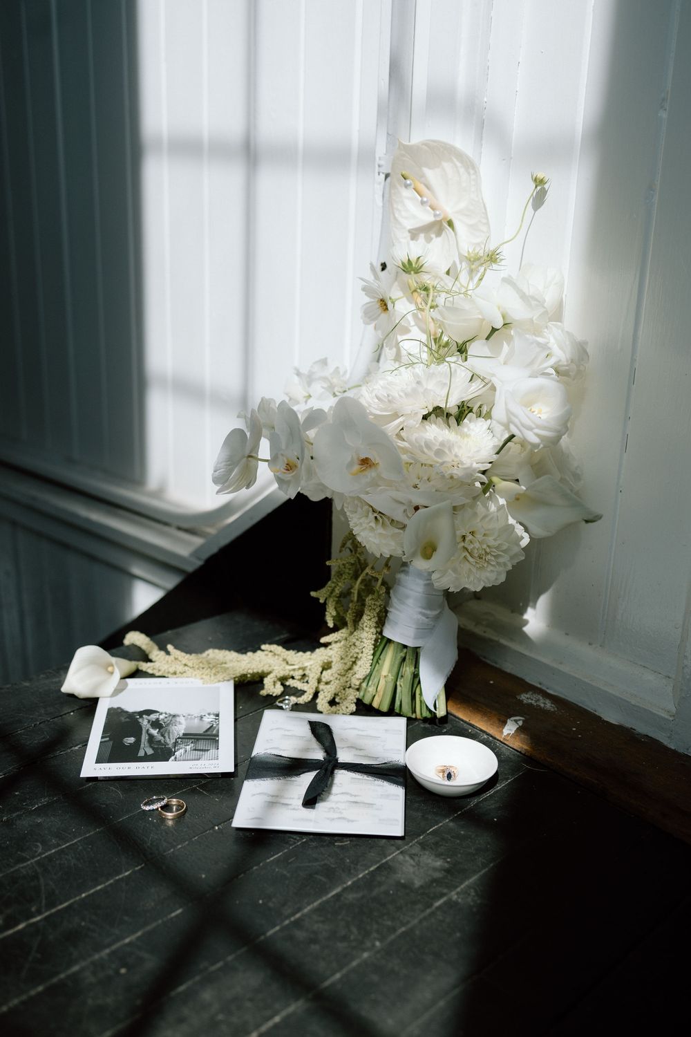 White flowers in a vase cast dramatic shadows on a dark floor near a window, creating a moody still life composition.