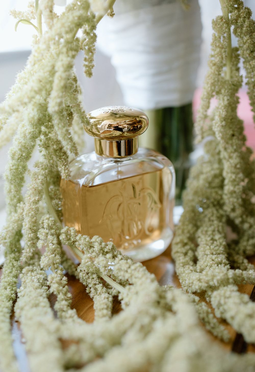 Gold perfume bottle nestled among delicate white astilbe flowers in soft focus.