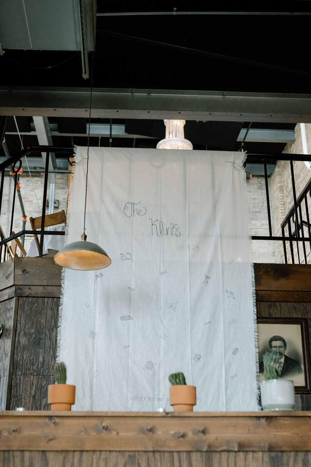A rustic wedding backdrop with white fabric, potted plants and vintage lighting fixtures.