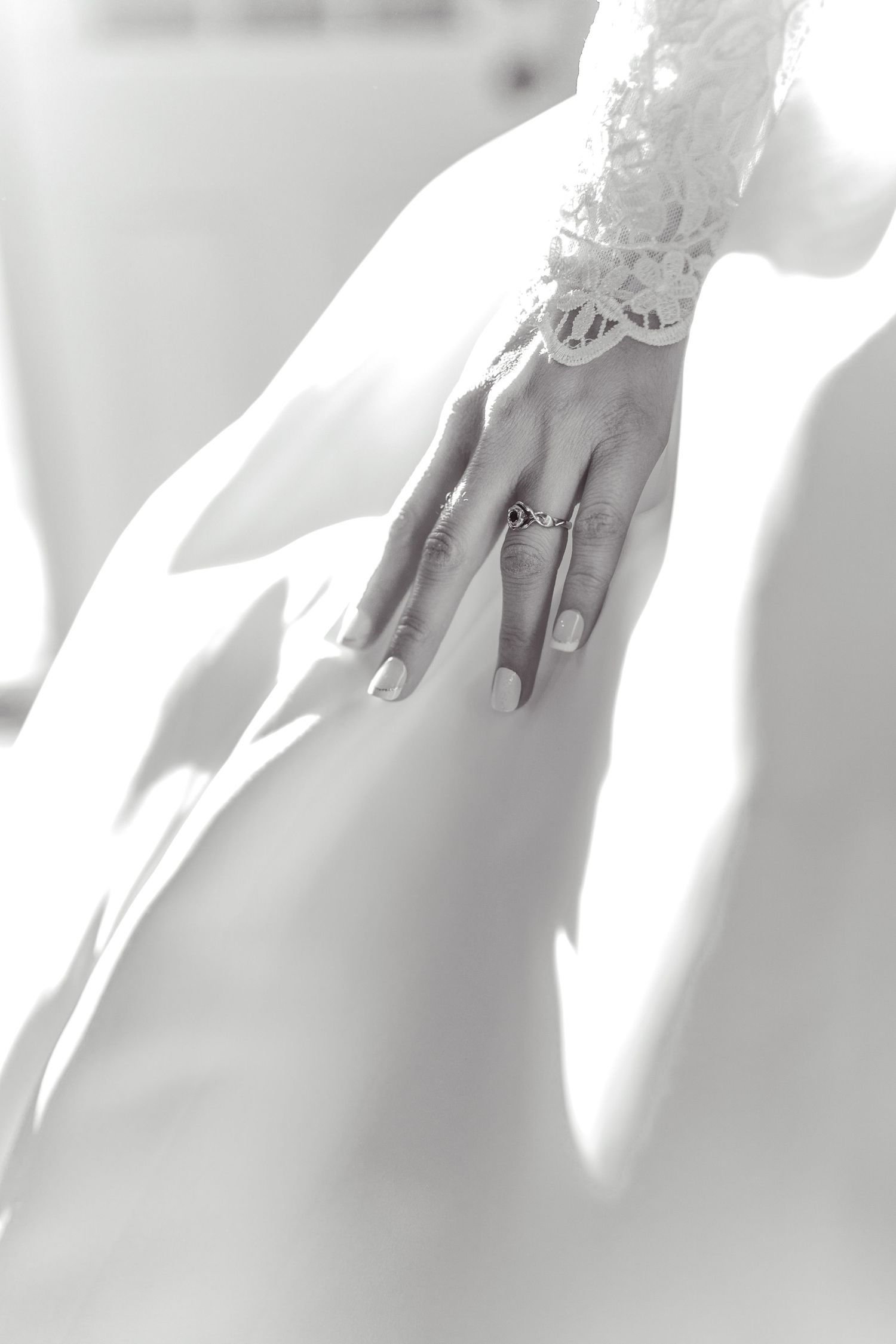 Black and white close-up of an elegant bridal hand with lace sleeve detail and wedding ring.