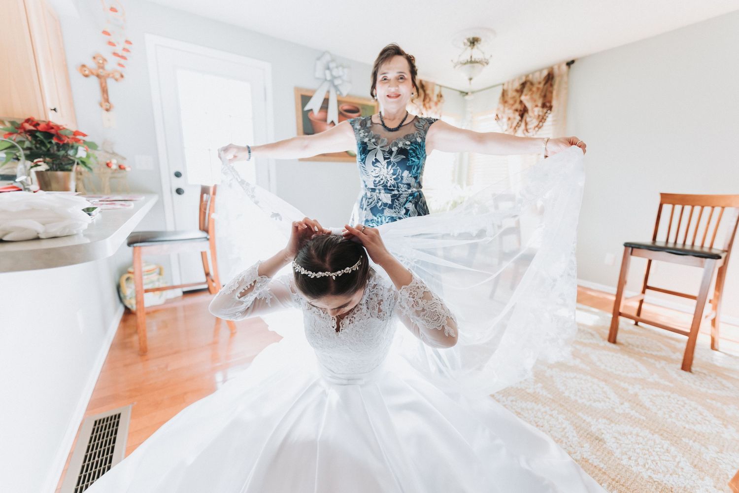 Wedding dress hangs elegantly against white wall with natural light streaming through windows.
