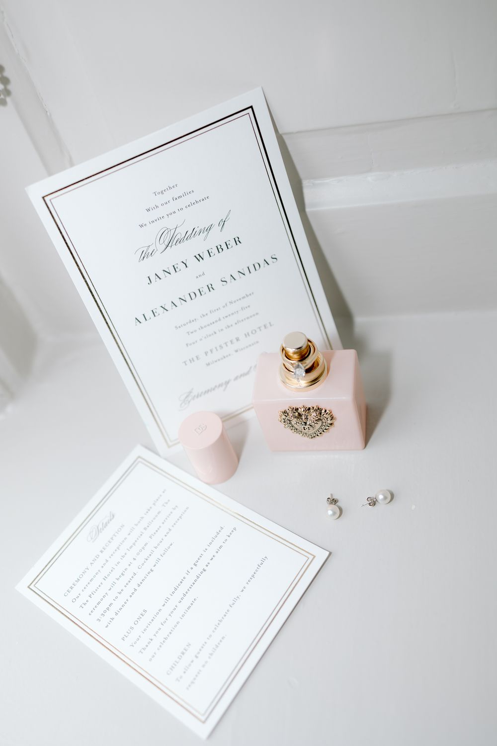 Elegant white wedding invitations with pink accents and rings displayed on light background.