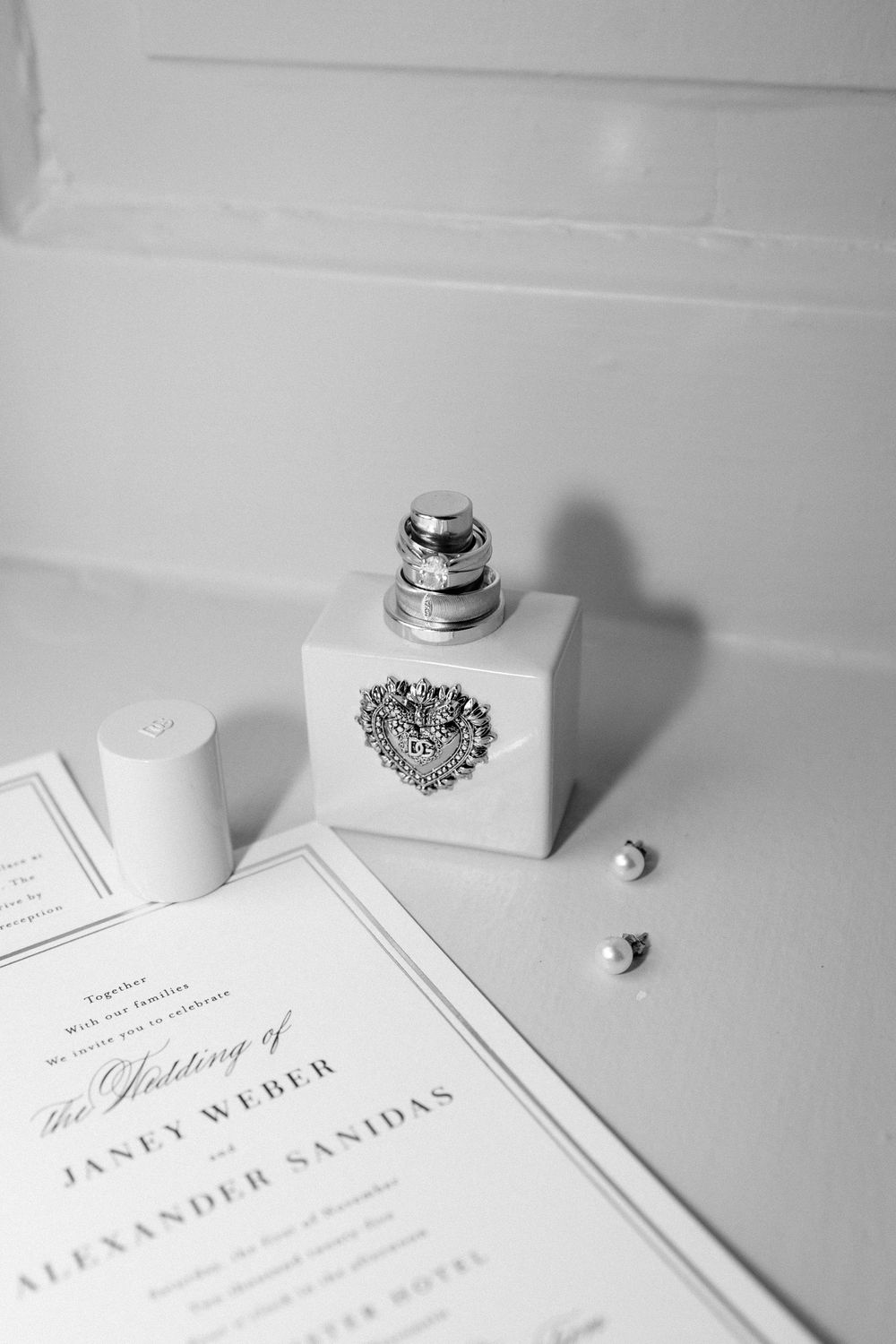 Black and white photo of classic wedding invitations and rings arranged on white surface.