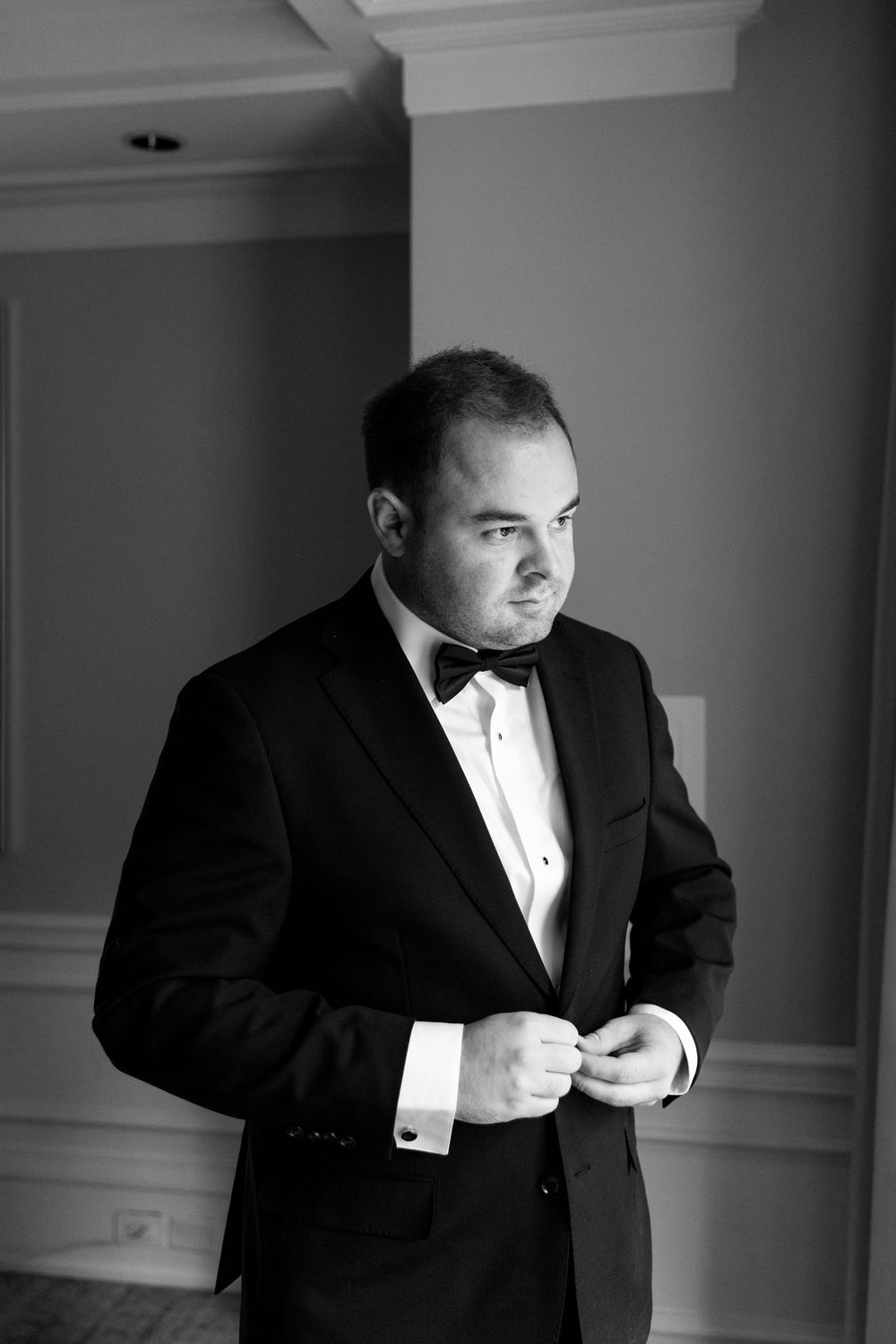 Black and white portrait of person adjusting bowtie in formal attire.
